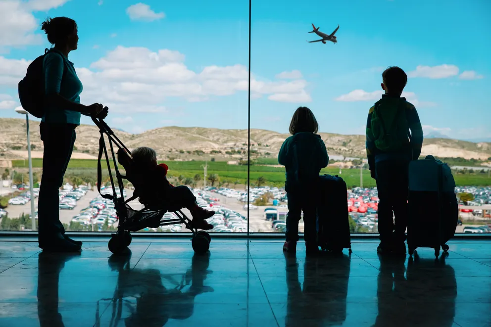 Una familia mirando un avión despegando desde la ventana de un aeropuerto. | Foto: Shutterstock