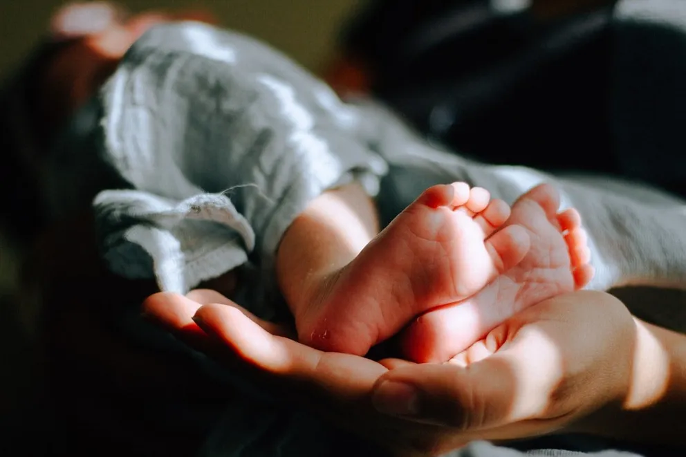 Hombre sosteniendo los pies de una bebé en su mano. | Foto: Unsplash