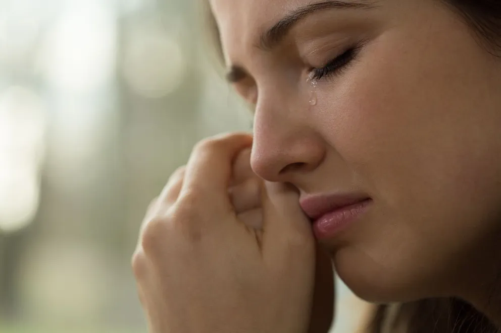Una mujer afligida con sus manos tocando su rostro mientras llora. | Foto: Shutterstock