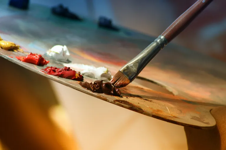Una persona mojando su pincel en pintura sobre una tabla para mezclar colores. | Foto: Pexels