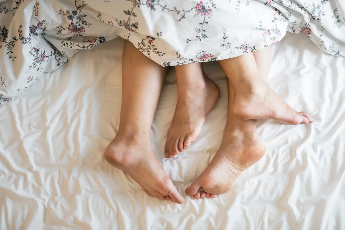 Erwachsene Beine, die aus einer Bettdecke ragen. | Quelle: Pexels