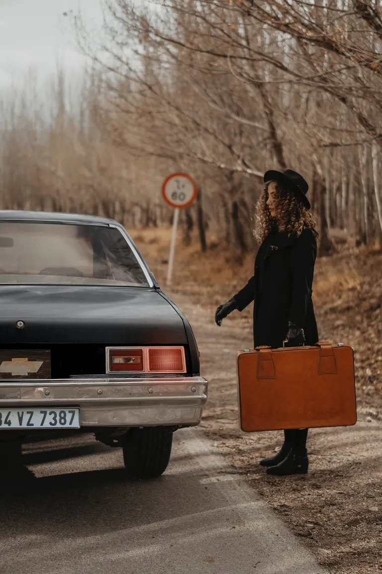 Una mujer con una maleta en su mano parada frente a un automóvil. | Foto: Pexels