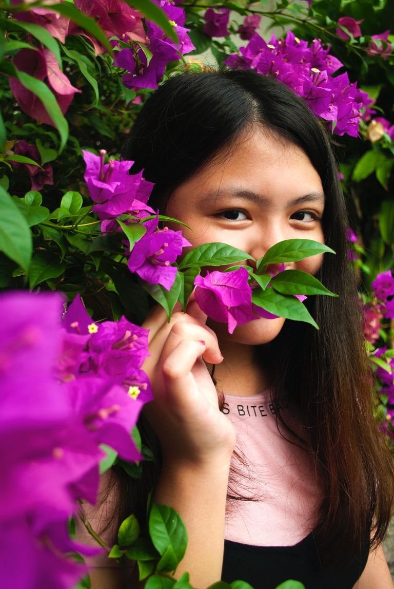 Una chica escondida detrás de un arbusto con flores. | Foto: Pexels