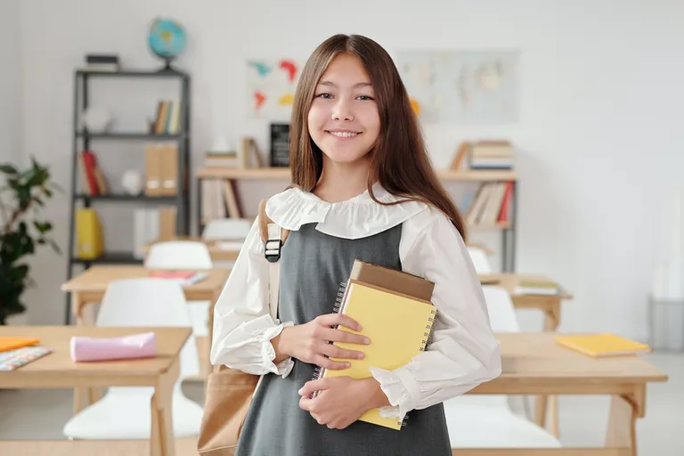 Una niña sonriendo mientras sostiene unas libretas. | Foto: Pexels