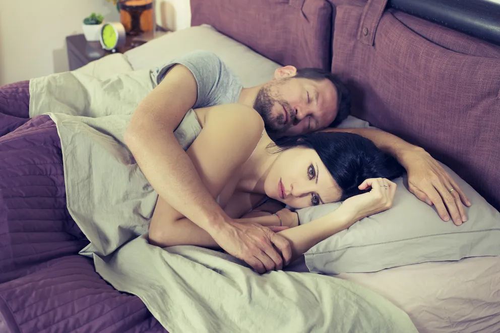 Una pareja recostada en una cama mientras la mujer está despierta y pensativa. | Foto: Shutterstock