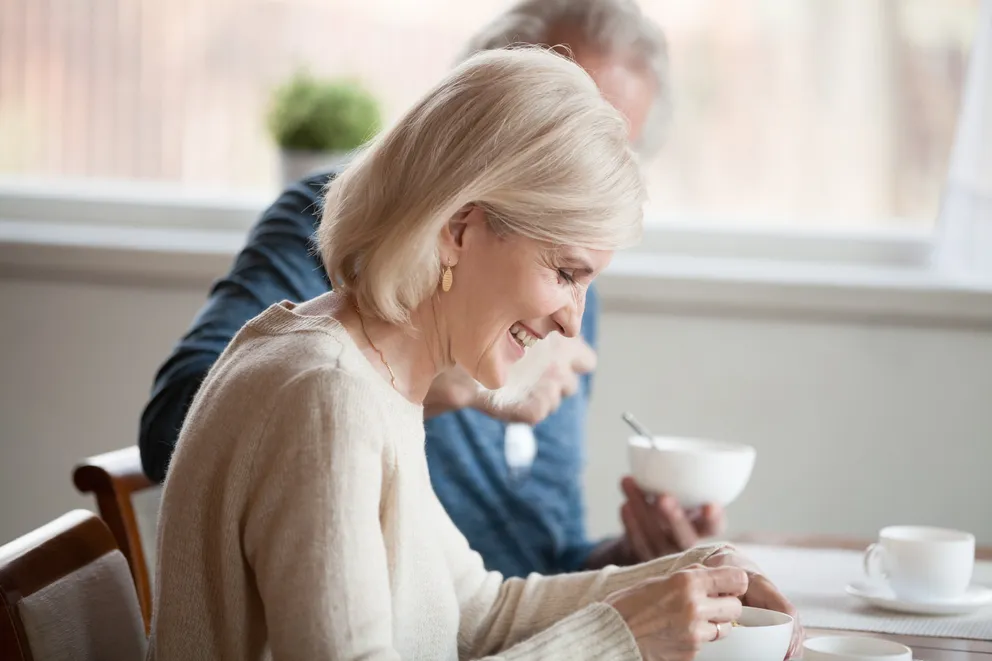 Una mujer sonriente sentada en una mesa junto a un hombre en una cafetería. | Foto: Shutterstock