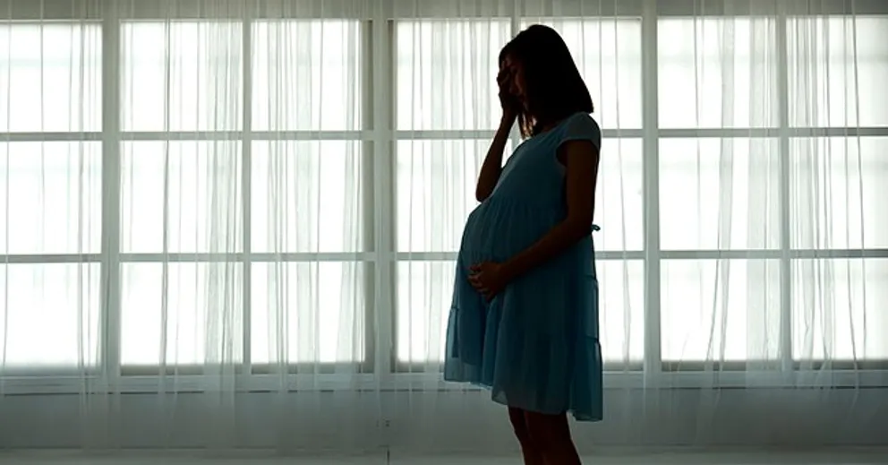 Mujer embarazada con la mano en su rostro junto a un ventanal. | Foto: Shutterstock