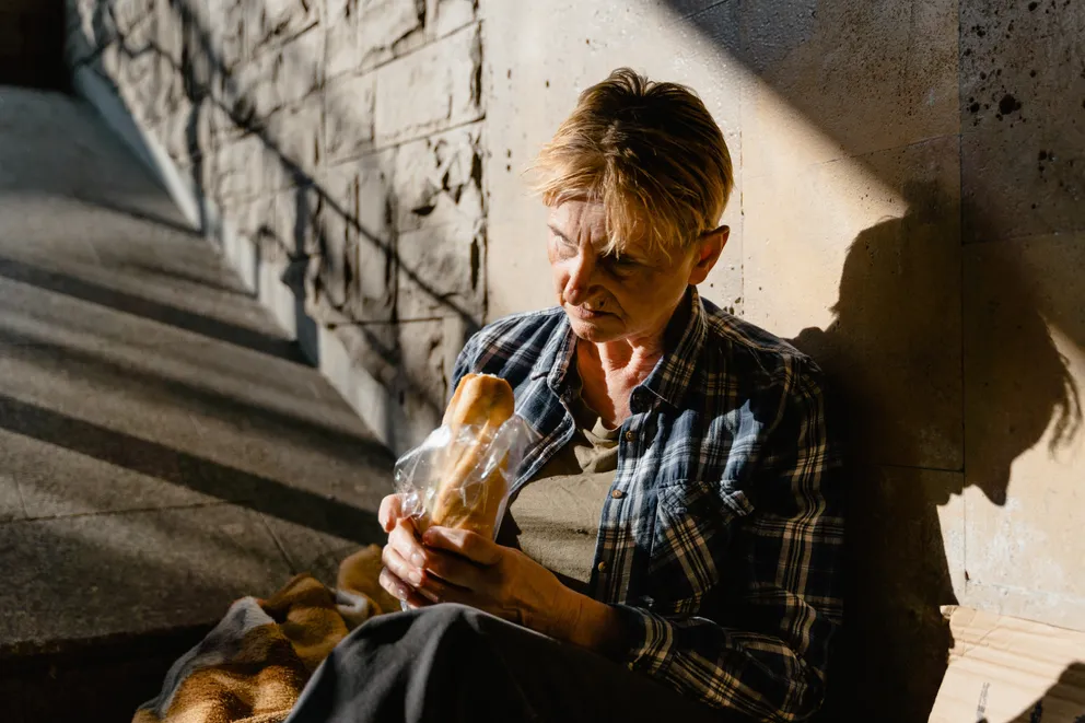 Una anciana sin hogar sentada en una escalera comiendo. | Foto: Pexels