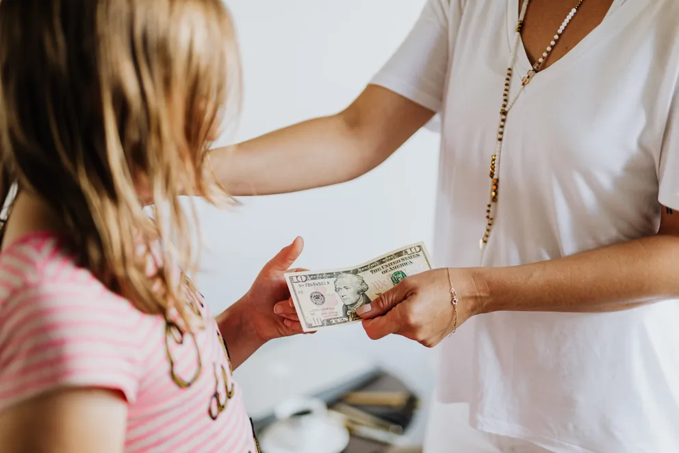 Una mujer entregando un billete de 10$ a una niña. | Foto: Pexels