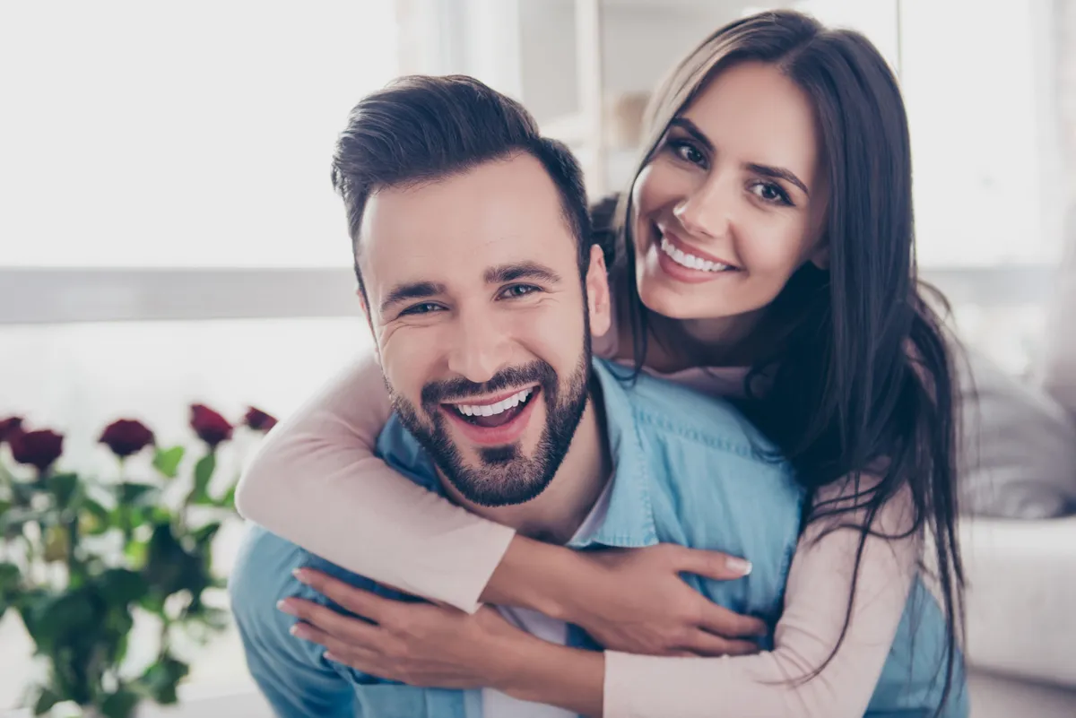 A couple smiling as the woman wraps his hands around her man. | Photo: Shutterstock