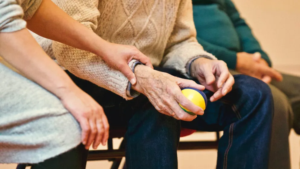 Anciano sosteniendo una pelota sentado junto a una persona. | Foto: Pexels