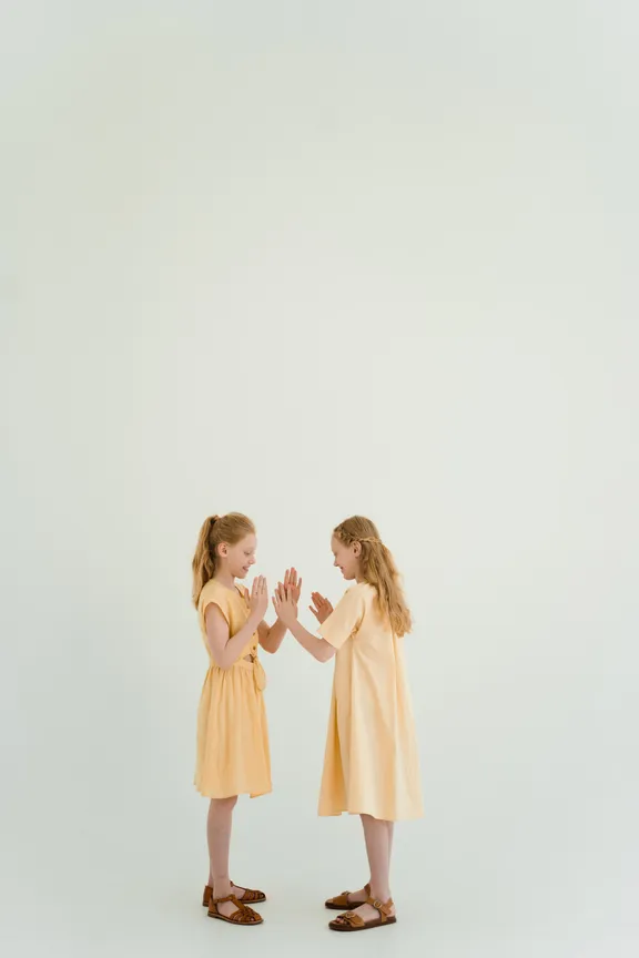 Dos niñas paradas una frente a la otra tocando sus manos. | Foto: Pexels