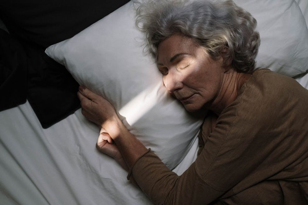 Una mujer mayor con los ojos cerrados recostada sobre una cama. | Foto: Pexels