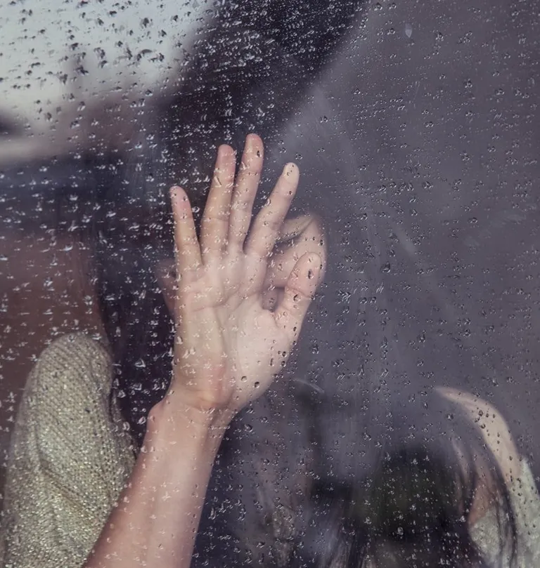 Mujer afligida recostada de una ventana en un día lluvioso. | Foto: Unsplash