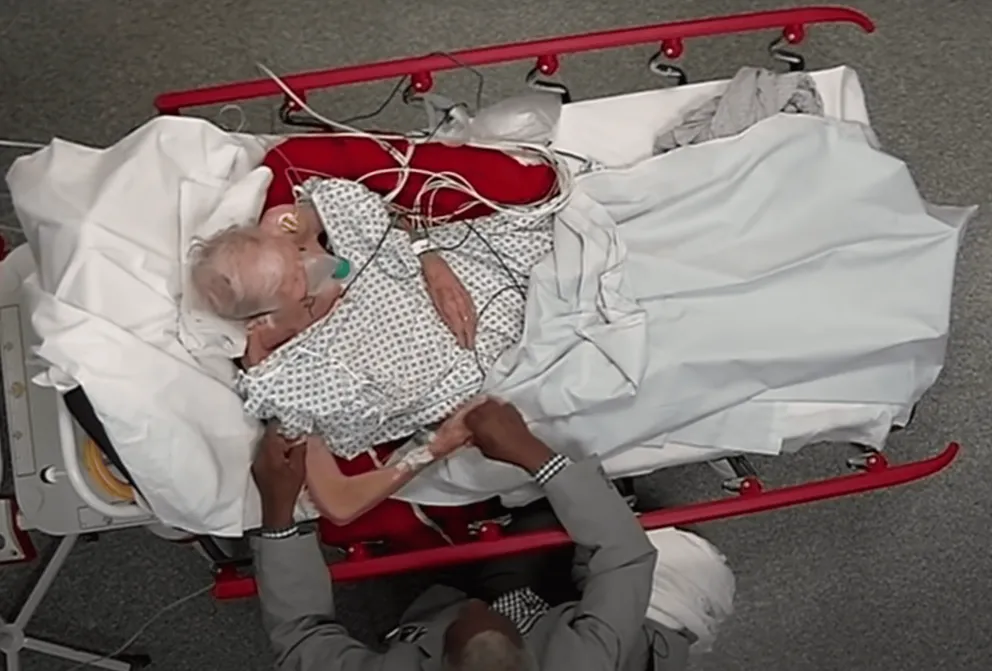 Andrew Augustus assis devant le lit d'hôpital de sa femme. | Source : youtube.com/Channel 4