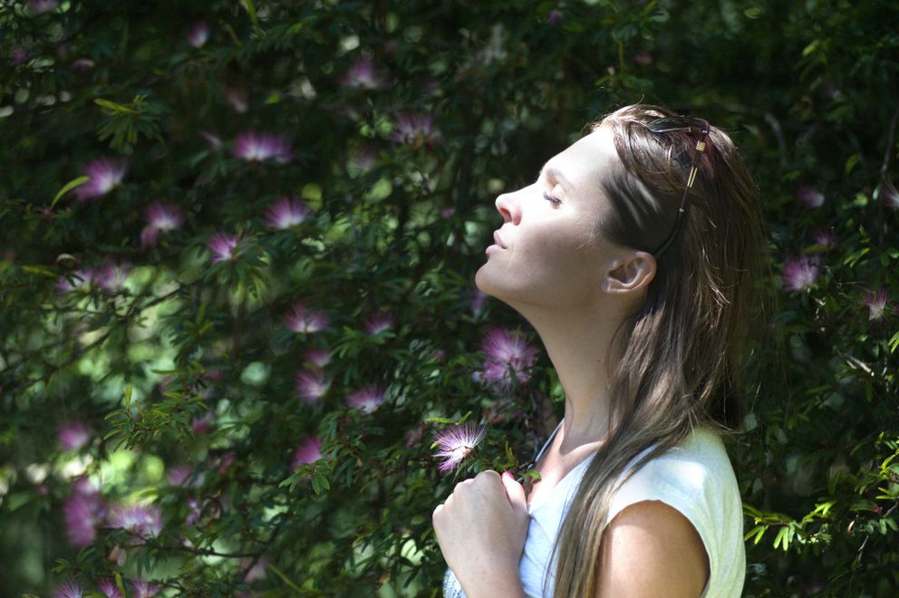 Una mujer pensativa con los ojos cerrados rodeada de arbustos. | Foto: Pexels