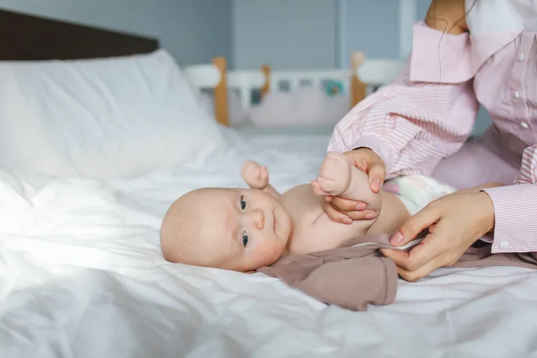 Mujer vistiendo a un bebé recostado sobre una cama. | Foto: Pexels