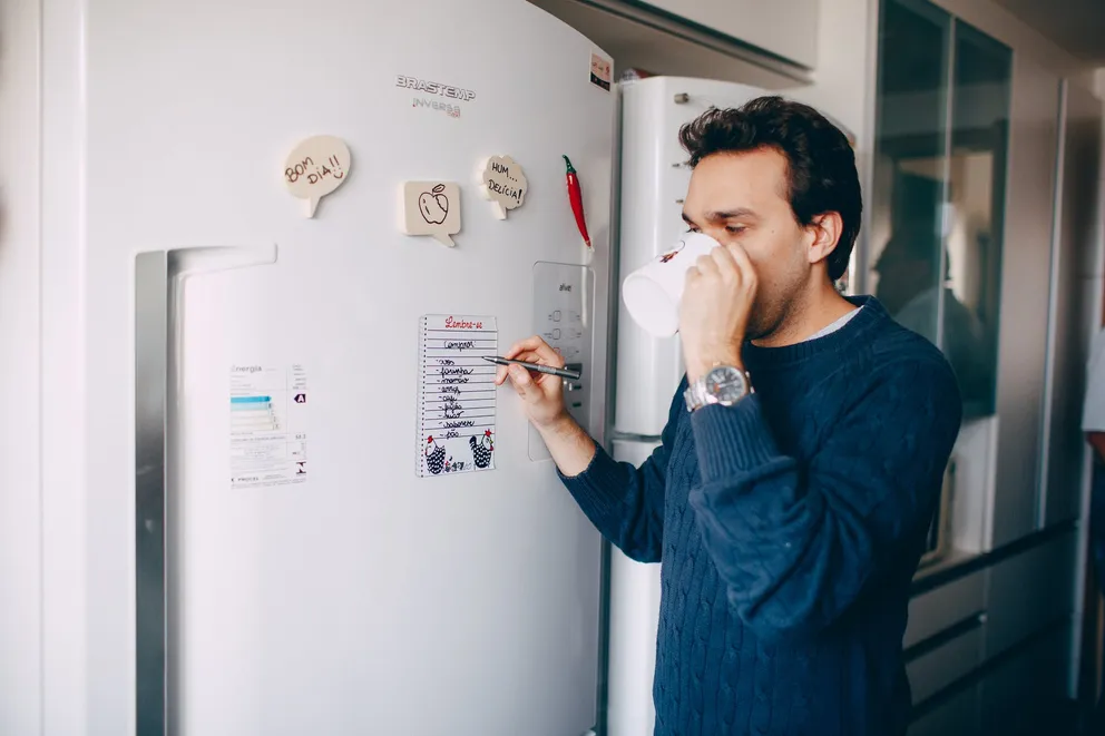 Hombre frente a un refrigerador tomando café. | Foto: Pexels
