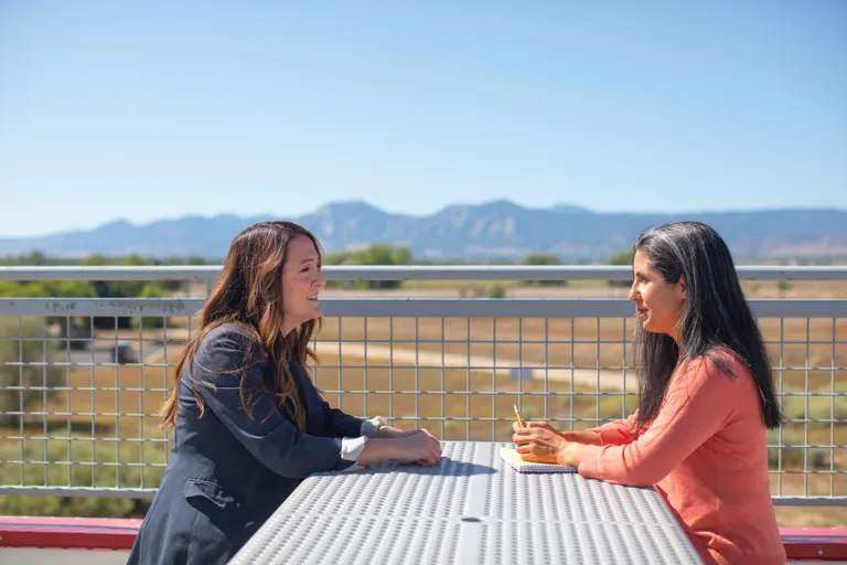 Una mujer sentada frente a una mesa mientras habla con otra mujer. | Foto: Pexels