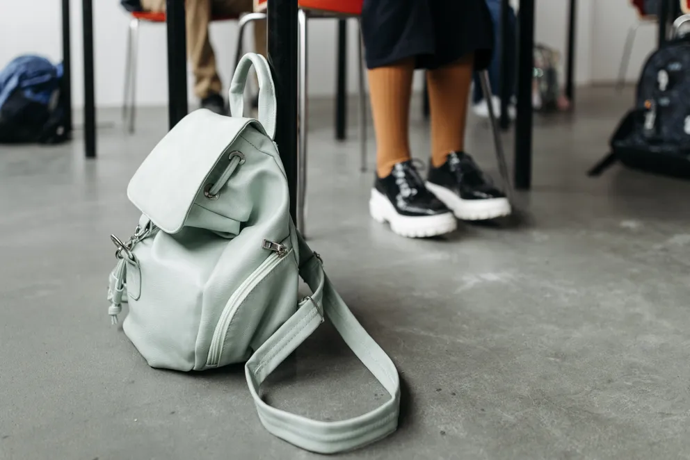 Bolso junto al escritorio de una estudiante en un salón de clases. | Foto: Pexels