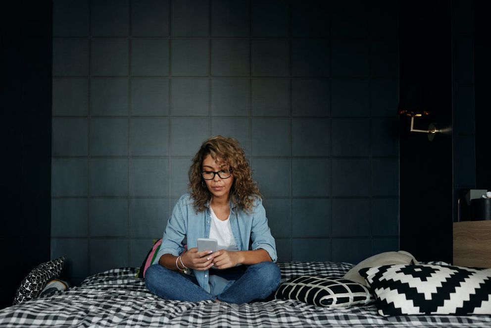 Una mujer sentada en su cama utilizando su teléfono celular. | Foto: Pexels