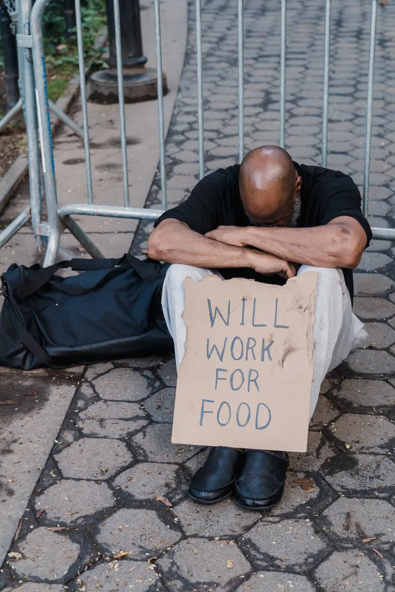 Un hombre sin hogar sentado en el suelo con su rostro entre sus brazos. | Foto: Pexels