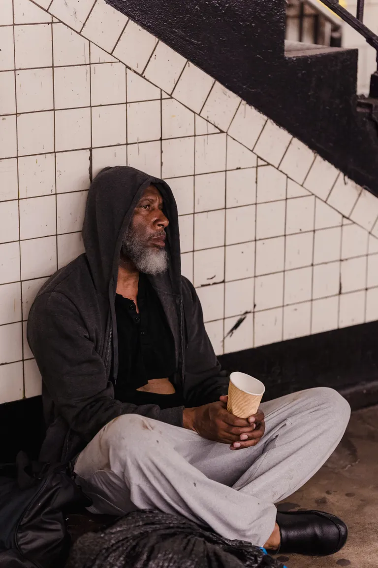 Un hombre mayor sin hogar sentado en el suelo cerca de unas escaleras. | Foto: Pexels