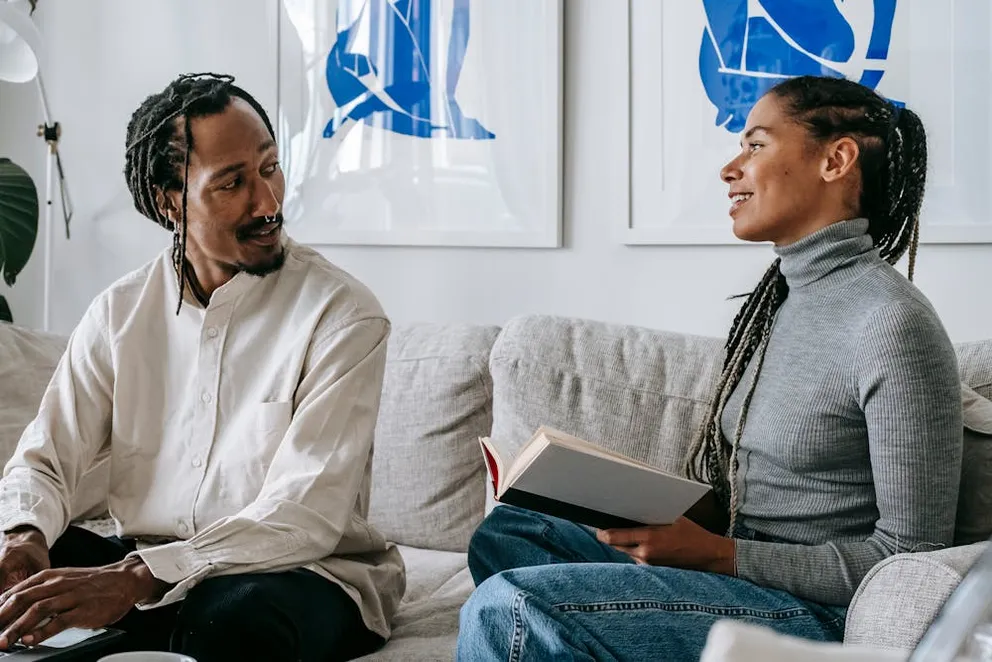Happy couple chatting while sitting on couch at home. | Photo: Pexels