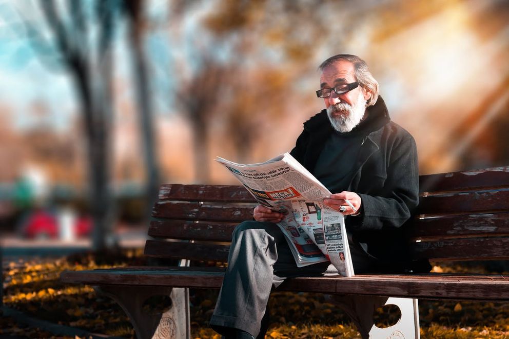 Un hombre mayor sentado en el banquillo de un parque leyendo el periódico. | Foto: Pexels
